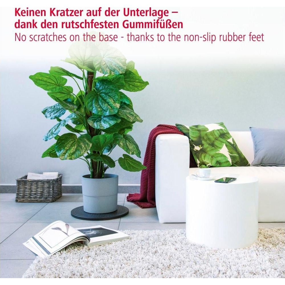 Ein großer grüner Kunstbaum neben einem Sofa mit Kissen und Decke.