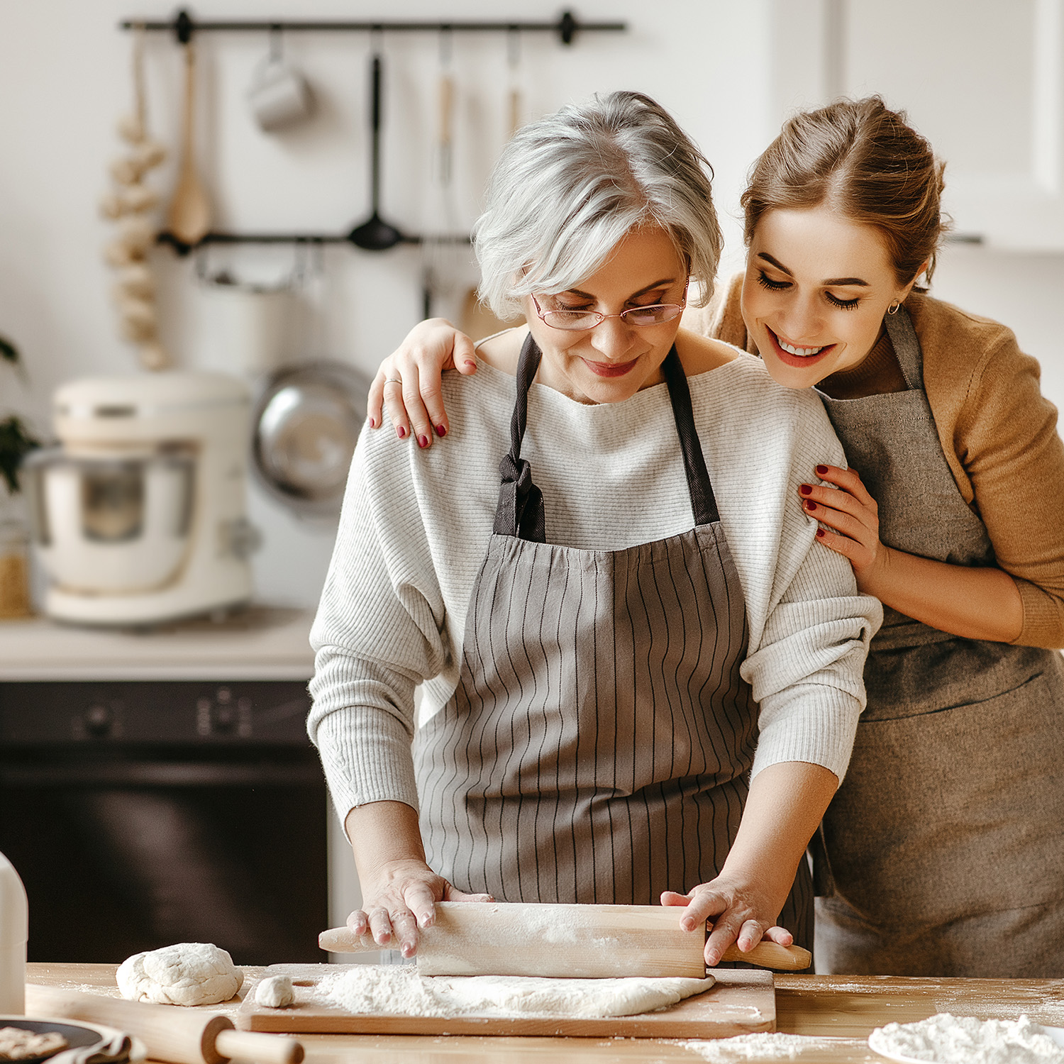 Donna e figlia cucinano insieme in cucina. L'anziana stende l'impasto.