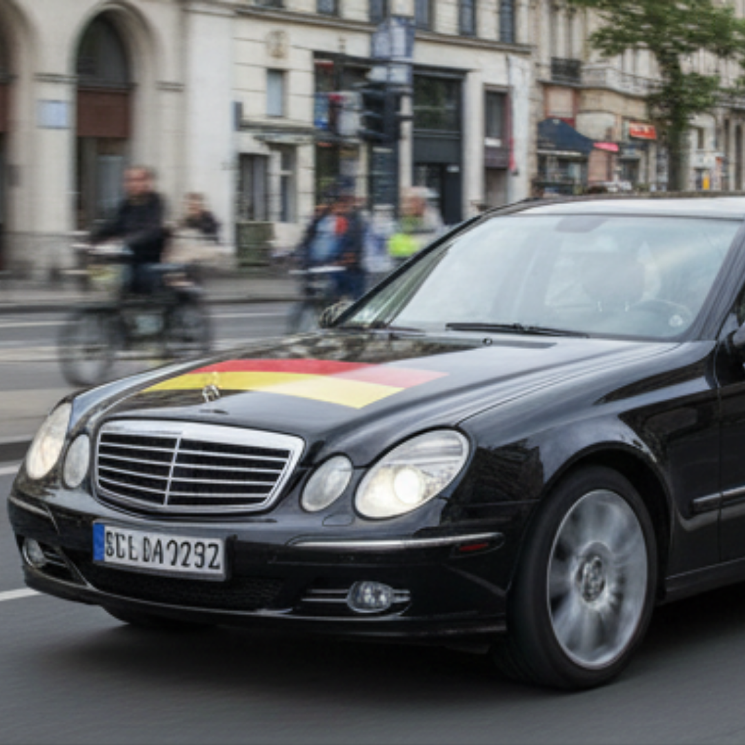 Schwarze Limousine mit deutscher Flagge auf der Motorhaube fährt auf der Straße.