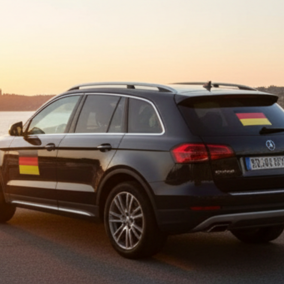 Schwarzer SUV mit deutschen Flaggen an der Seite und am Heck bei Sonnenuntergang.