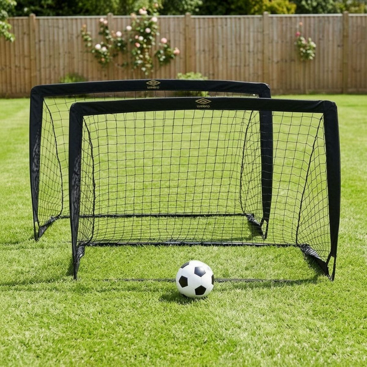 Zwei schwarze Umbro Fußballtore auf einem Rasen mit einem Fußball davor.