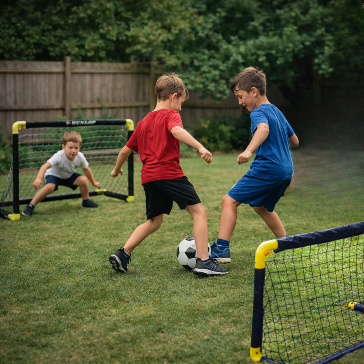 Drie jongens voetballen in een tuin met twee doelen.