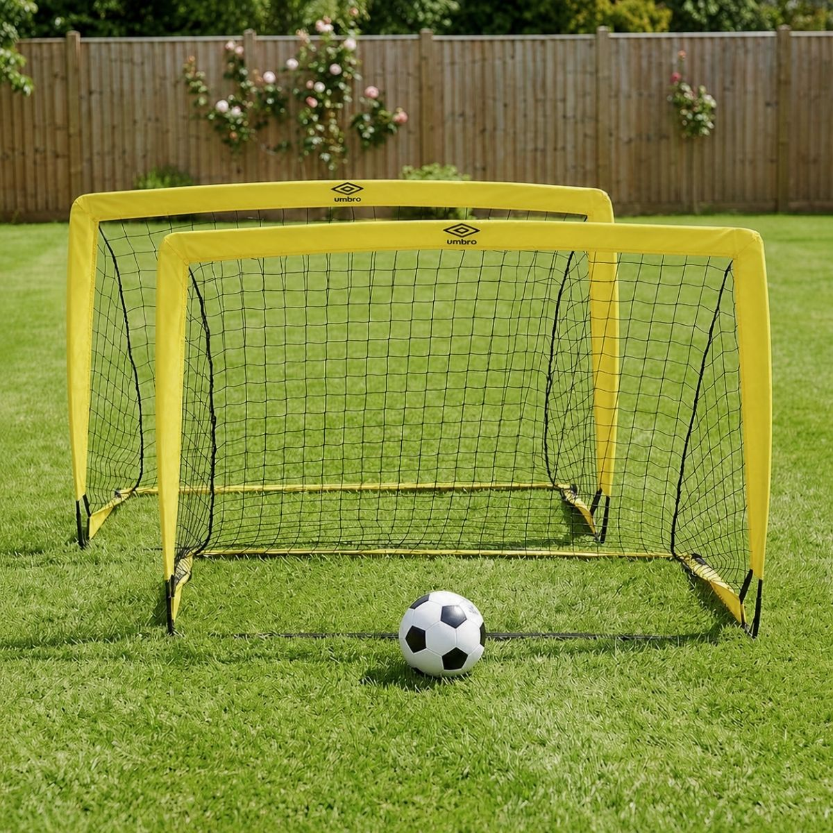 Zwei gelbe Umbro-Fußballtore und ein Fußball auf einem grünen Rasen.