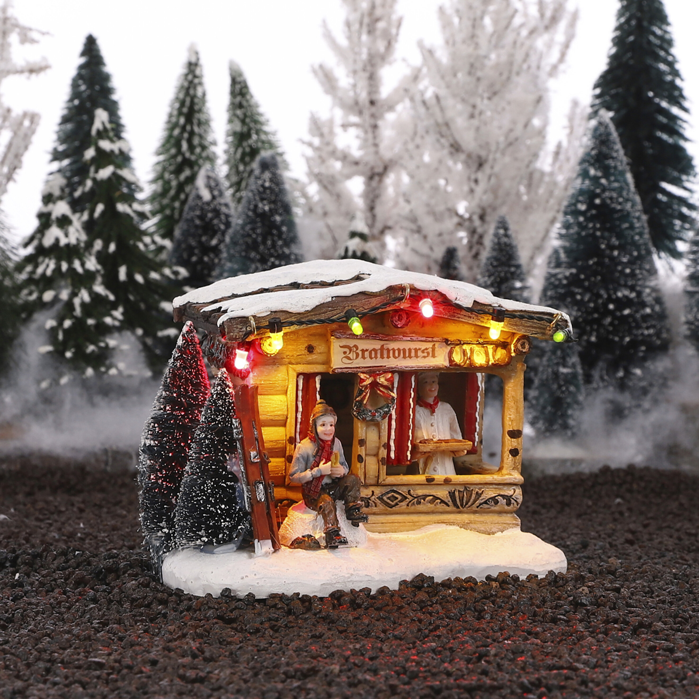 Een miniatuur kerstmarktkraam met twee figuren, verlicht, bedekt met sneeuw.