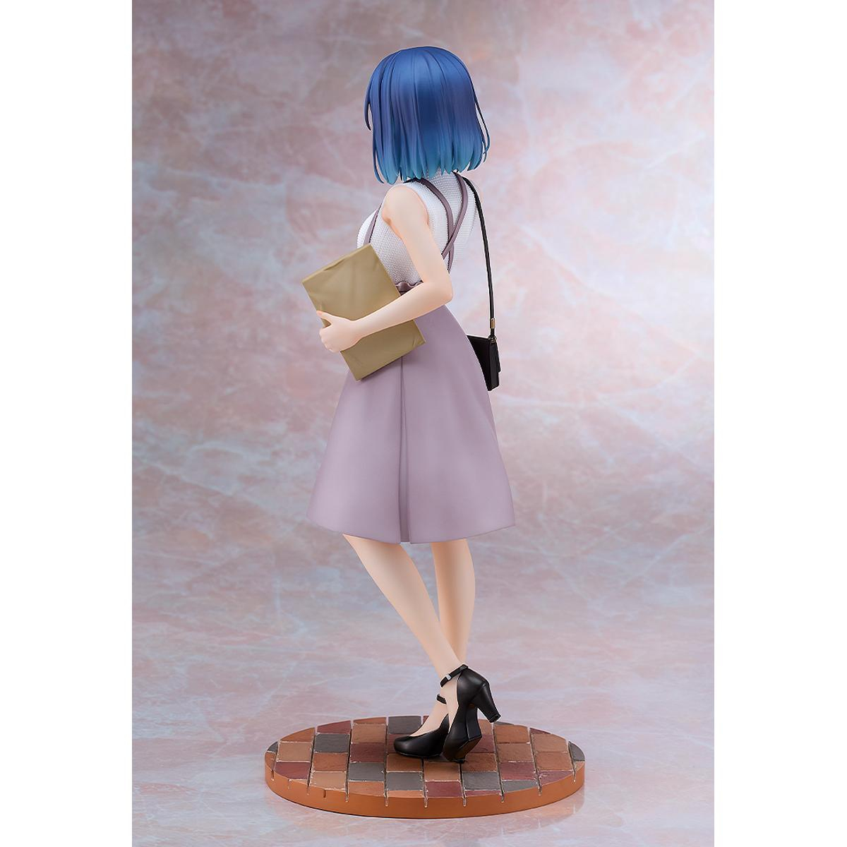 Figura de mujer con pelo azul sosteniendo un libro, de pie sobre base colorida.