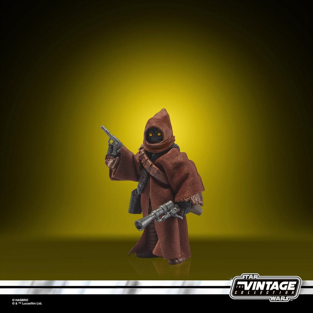Una figura Jawa con capucha y túnica marrón sostiene dos armas.