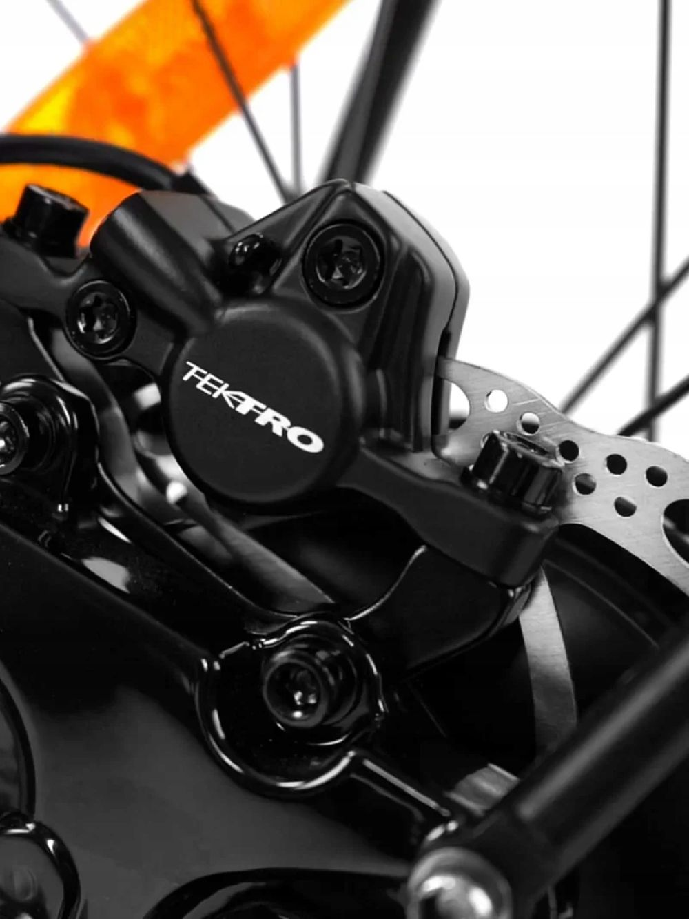 Primo piano di un freno per bicicletta Tektro nero con disco metallico. Telaio arancione sullo sfondo.
