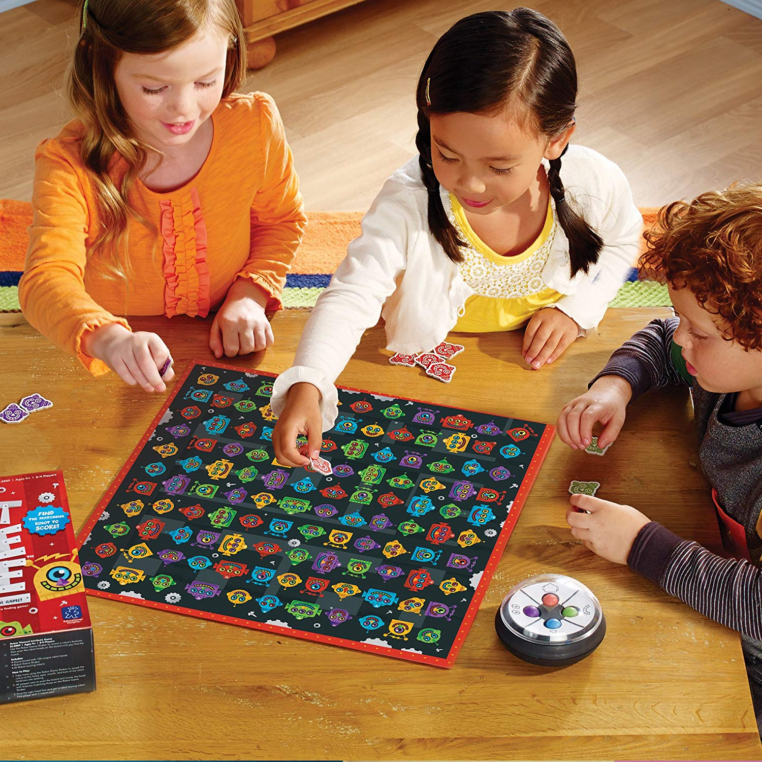 Tres niños juegan un juego de mesa con robots coloridos en una mesa de madera.