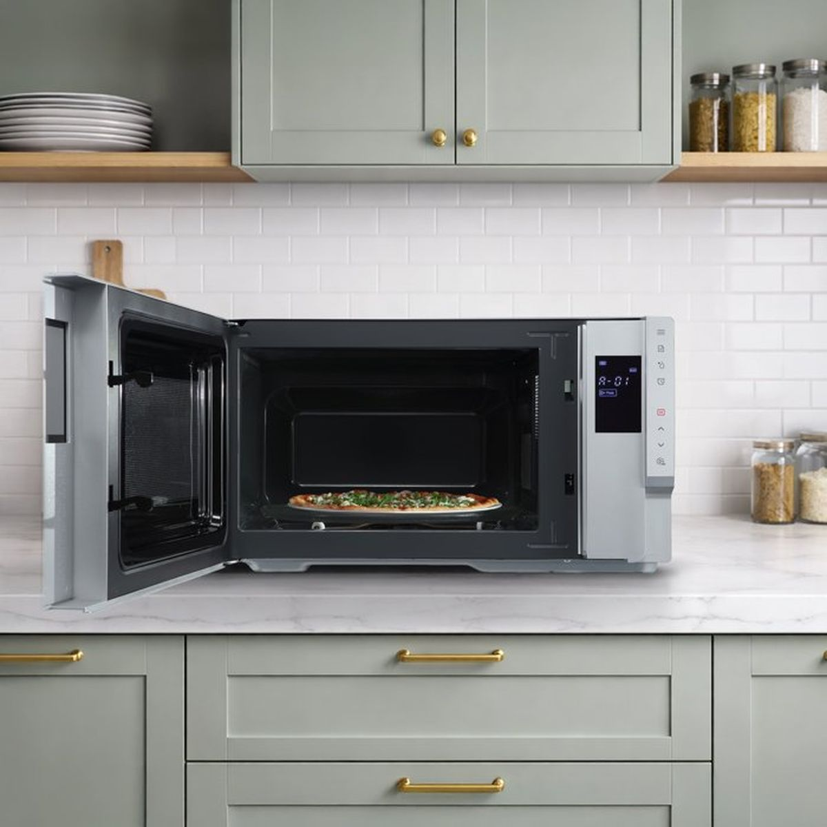 Un forno a microonde argentato aperto con una pizza all'interno, su un piano di lavoro in marmo.