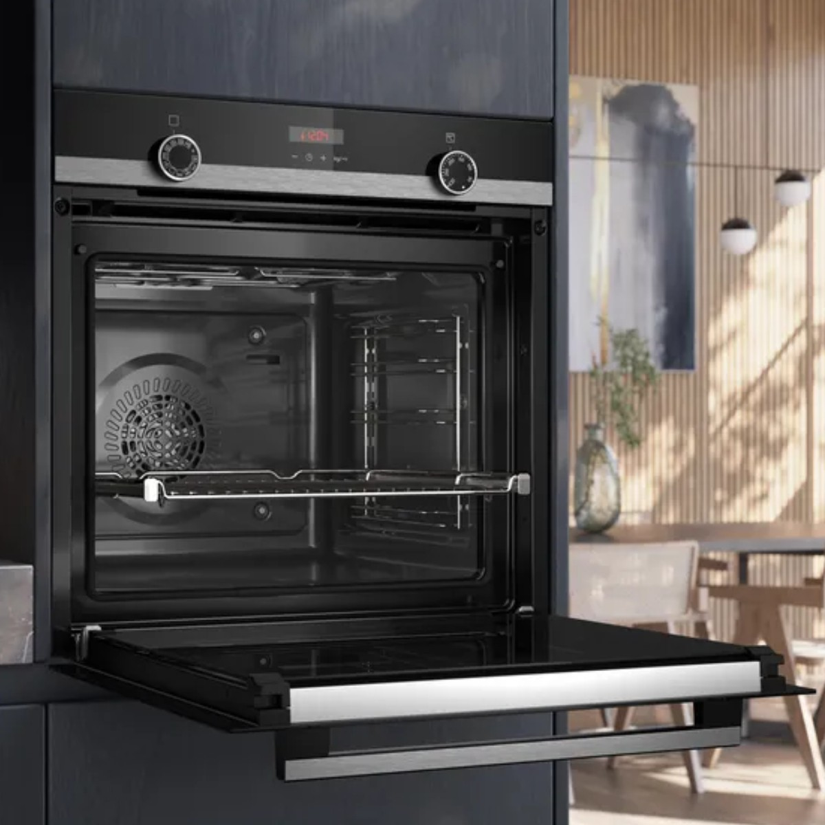 Un forno da incasso moderno con porta aperta, ventola e griglia interne. Tavolo da cucina sullo sfondo.