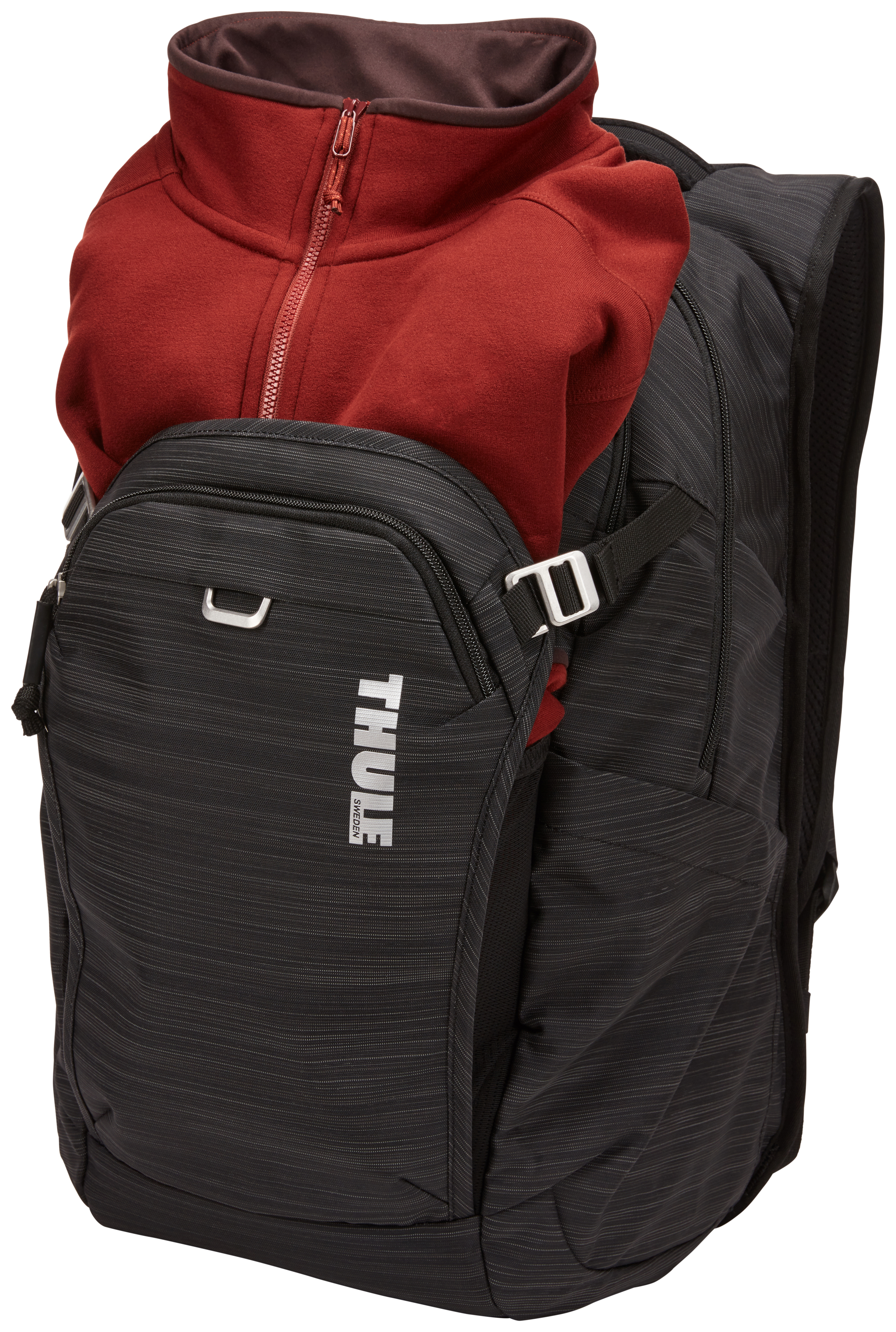 Una giacca in pile rossa è parzialmente inserita in uno zaino nero con logo Thule.