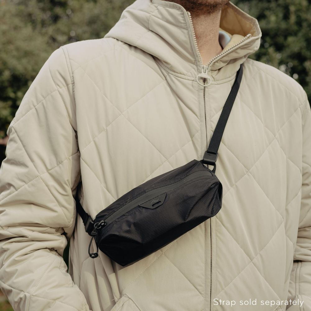 Man in een gewatteerde, crèmekleurige jas met zwarte crossbody tas.