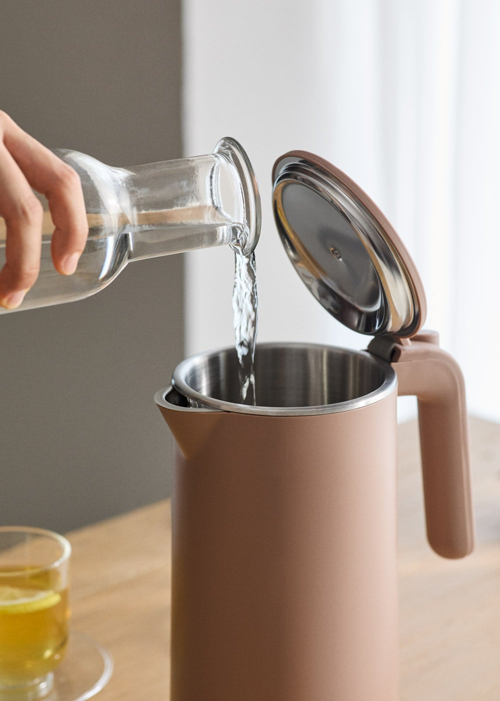 Se vierte agua de una botella de vidrio en una tetera beige.