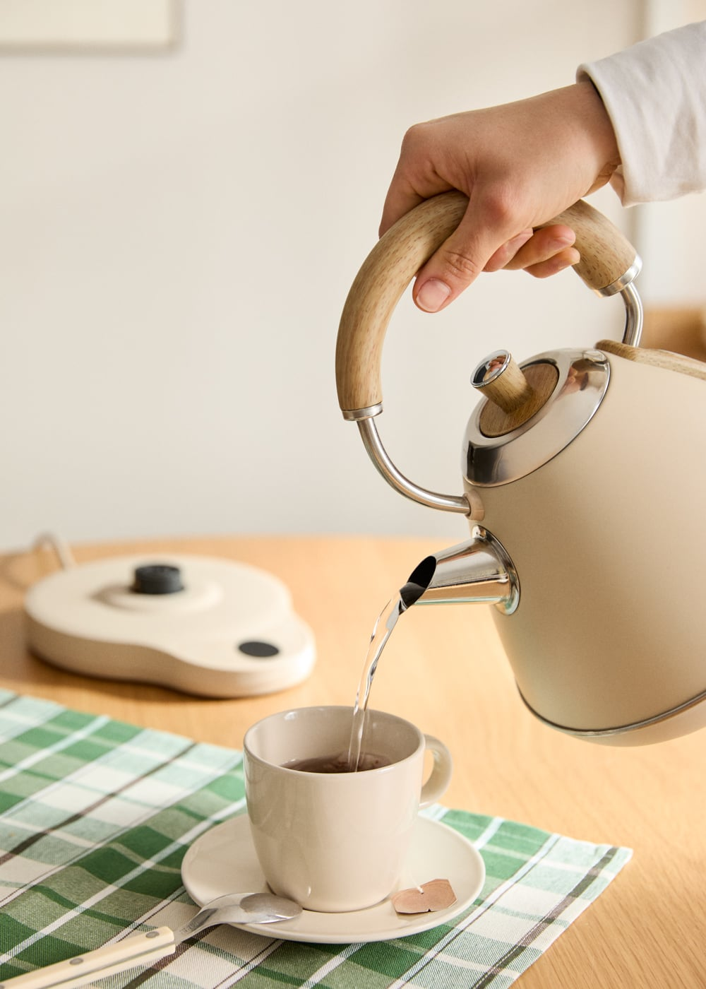 Una mano vierte agua de una tetera color crema en una taza.