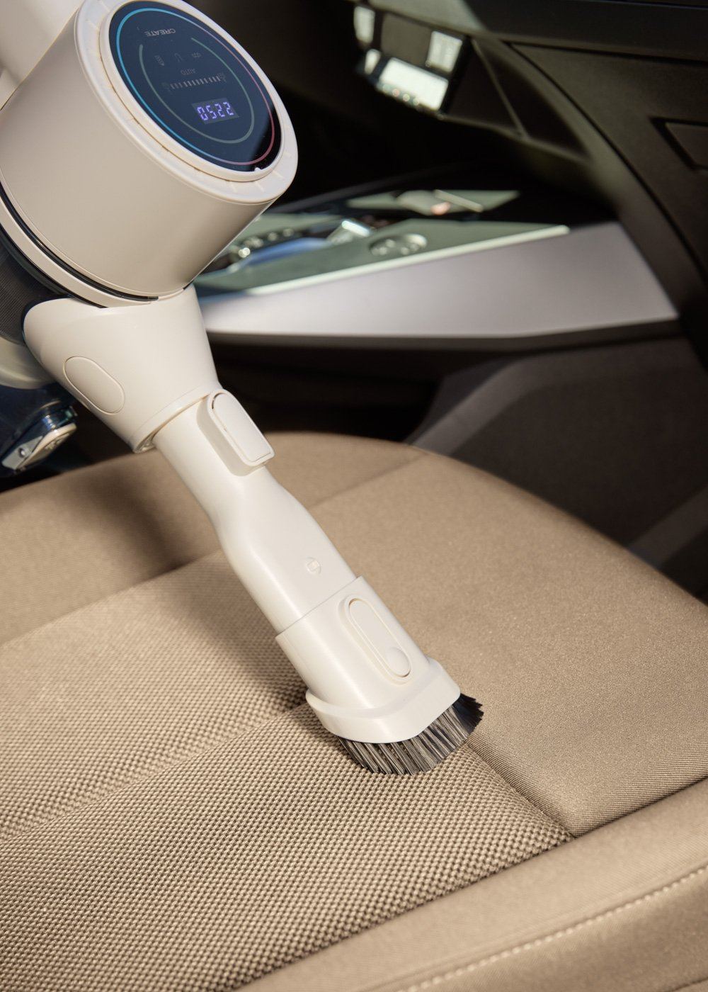 Una aspiradora blanca de mano limpia un asiento de coche beige.