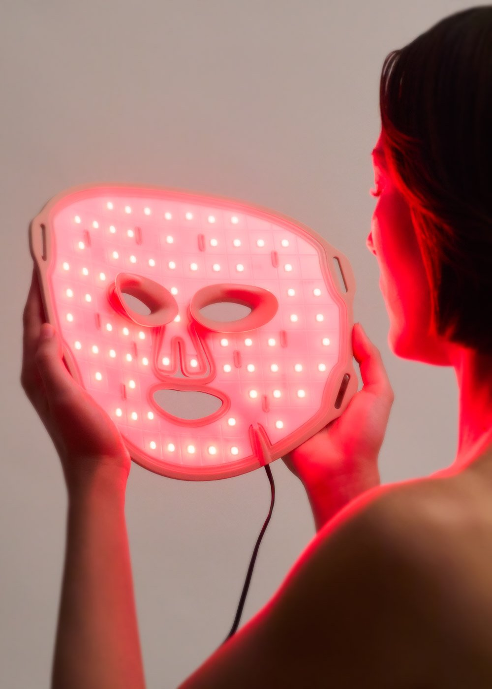 Una persona sostiene una mascarilla con luces LED rojas.