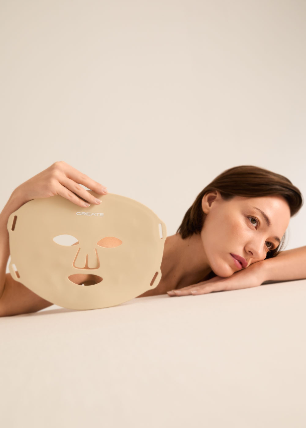 Una mujer yace de lado, sosteniendo una mascarilla facial beige.