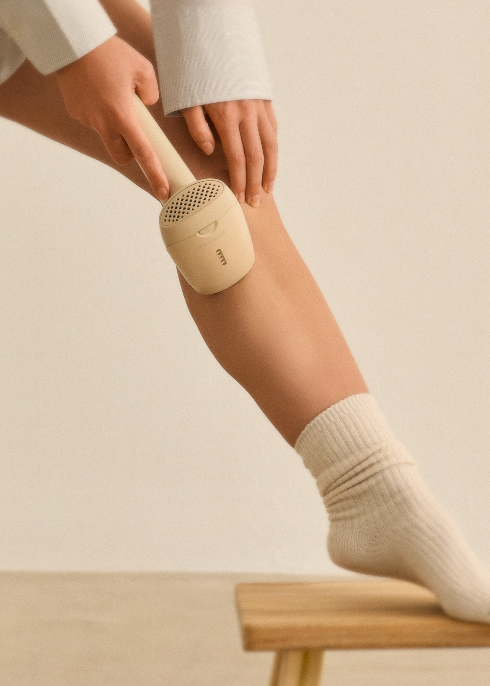 Una mano sujeta un depilador beige en la rodilla de una persona con calcetines beige.