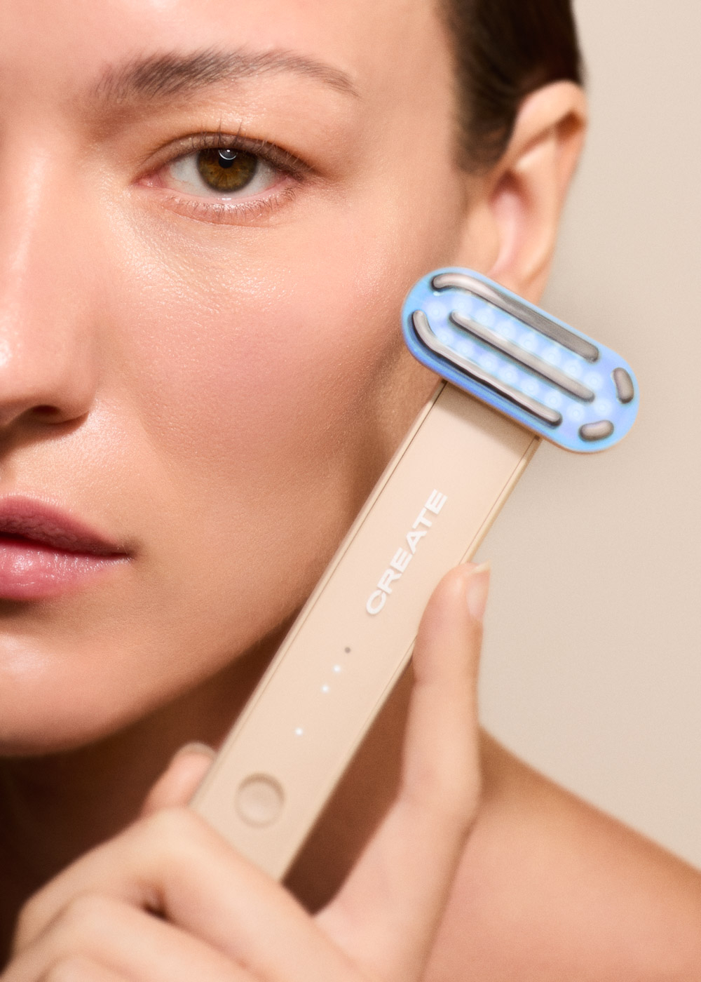 Una mujer aplica un dispositivo facial LED azul apoyado en su mejilla.