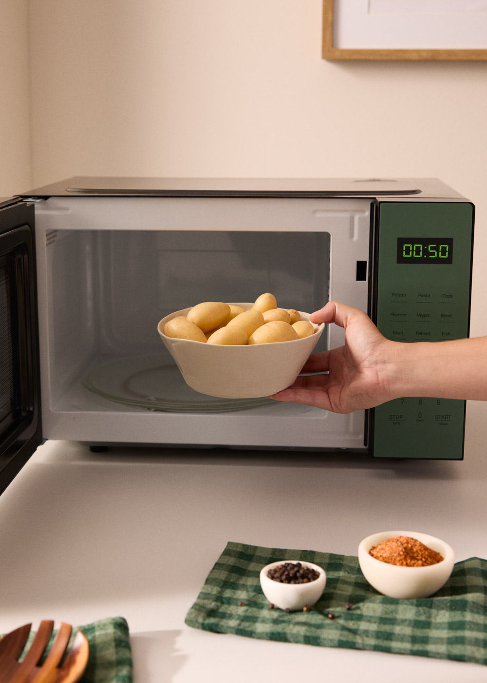 Una mano coloca un cuenco de patatas en un microondas. Temporizador 00:50.