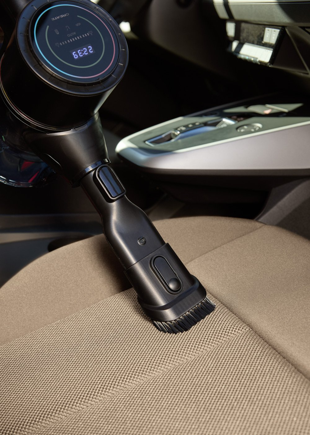Una aspiradora negra de mano limpia un asiento de coche beige.