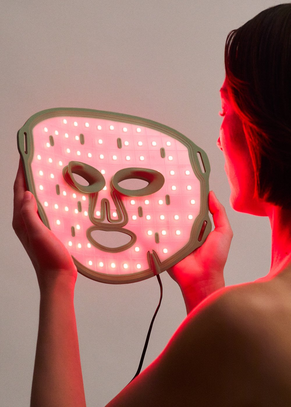 Una mujer sostiene una mascarilla con luces rojas frente a su rostro.