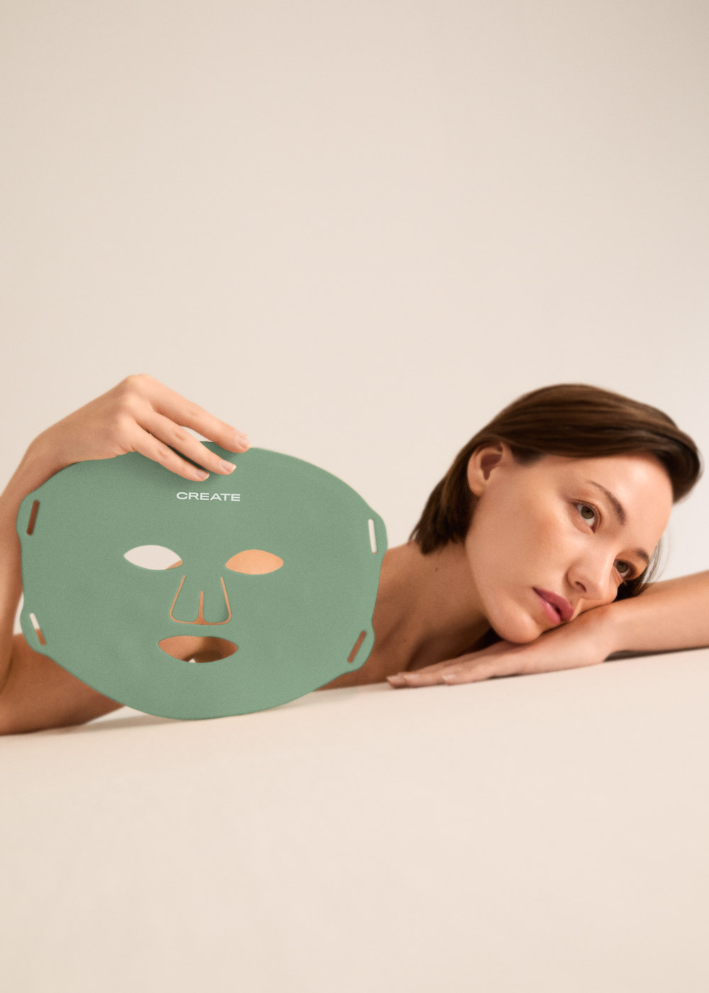 Una mujer con una mascarilla facial verde junto a su rostro.