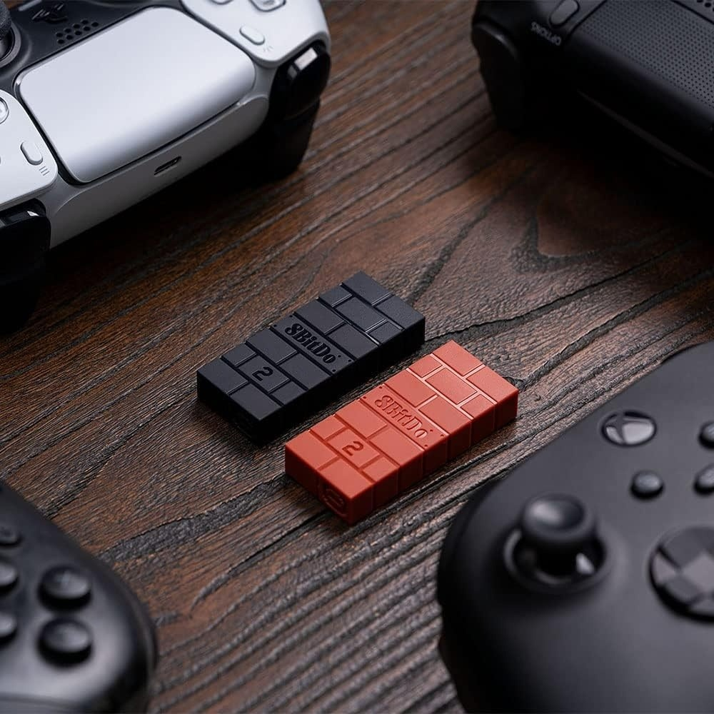 Zwei kleine USB-Sticks, rot und schwarz, auf einem Holztisch mit Controllern.