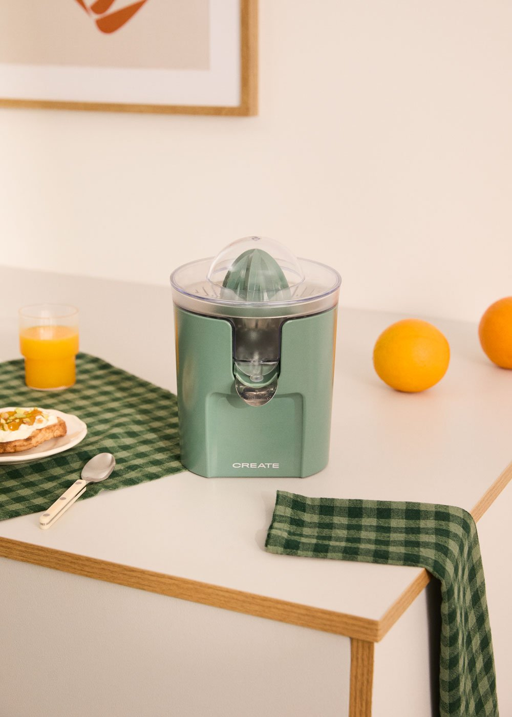 Un exprimidor verde está sobre una encimera blanca junto a naranjas y tostadas.