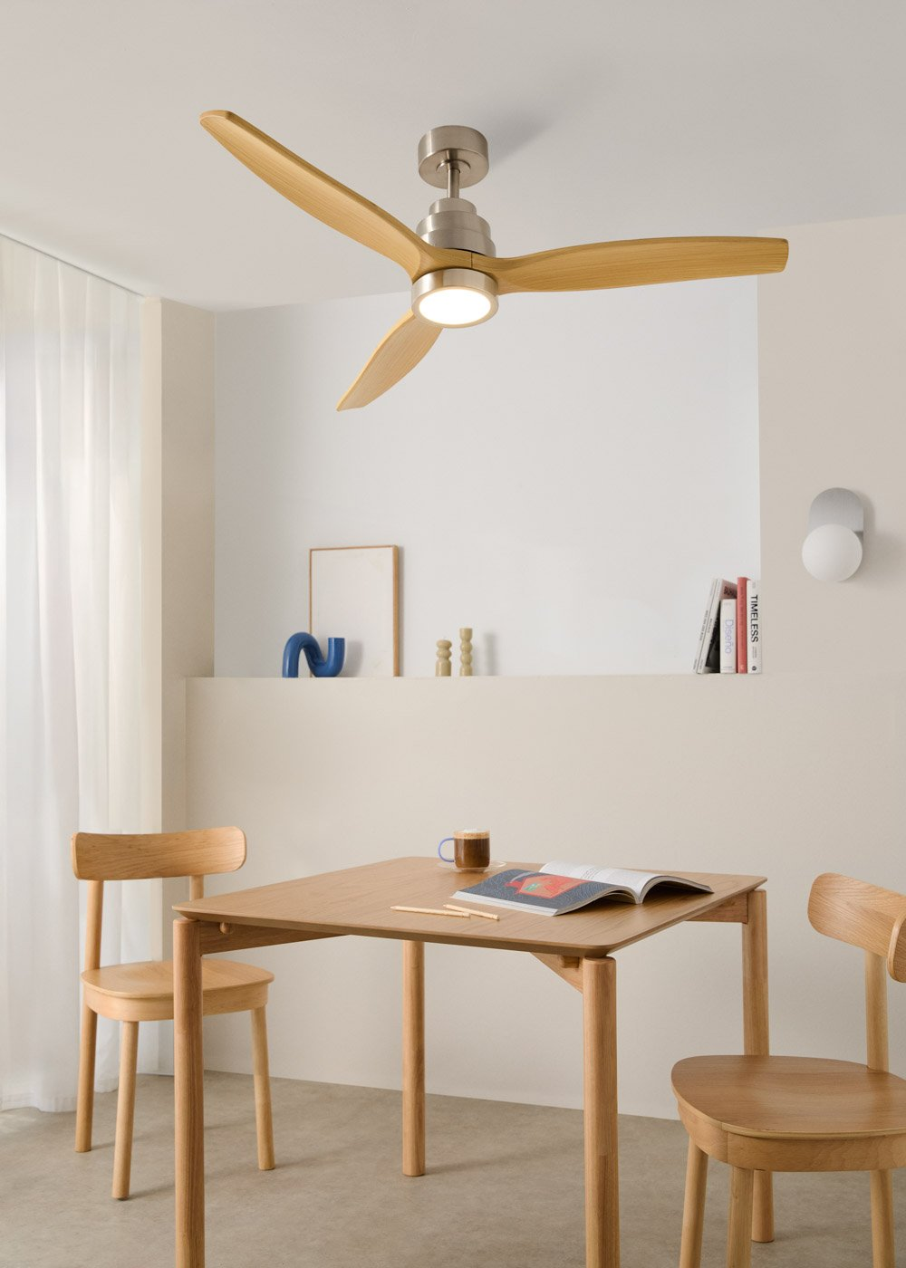 Un ventilador de techo con aspas de madera y luz sobre una mesa de madera con sillas.