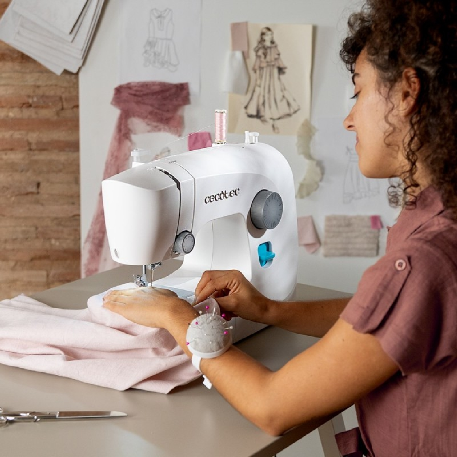 Una mujer con pelo rizado cose tela rosa en una máquina de coser.