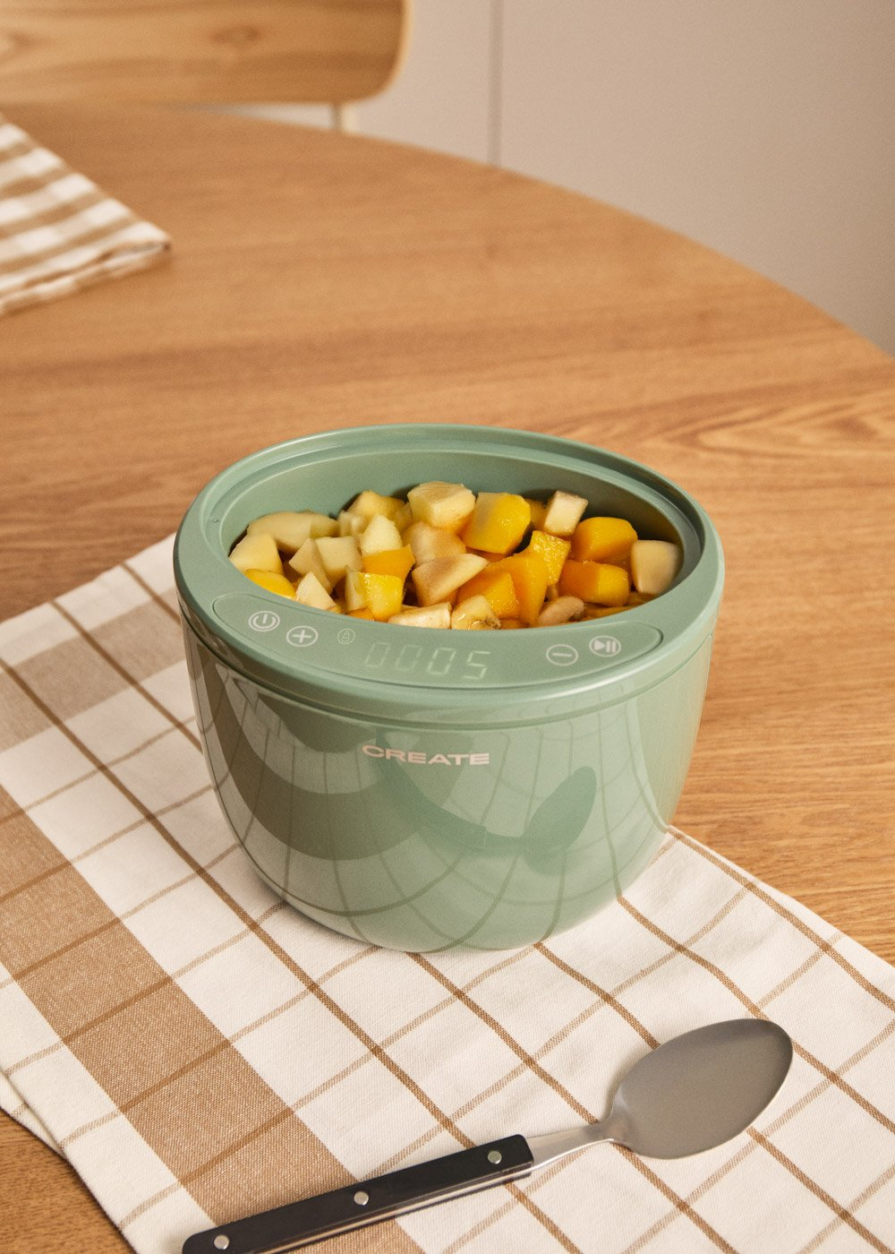 Un cuenco verde con fruta troceada sobre un paño a cuadros en una mesa de madera.
