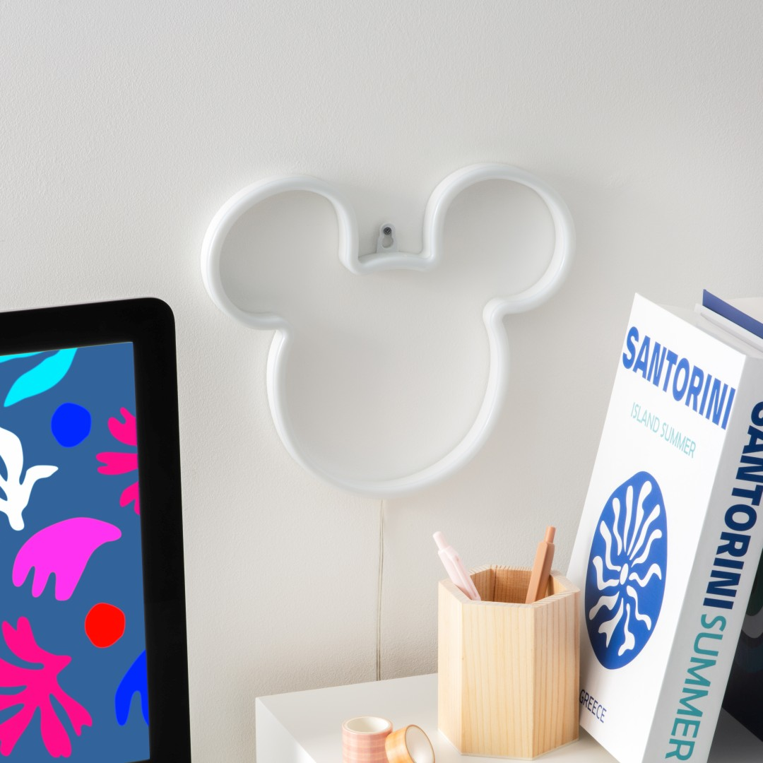 Biała lampa neonowa Myszki Miki na ścianie, obok tabletu i książek.