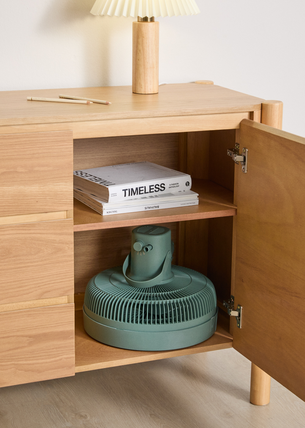 Armario de madera con puerta abierta, libros y un ventilador verde.