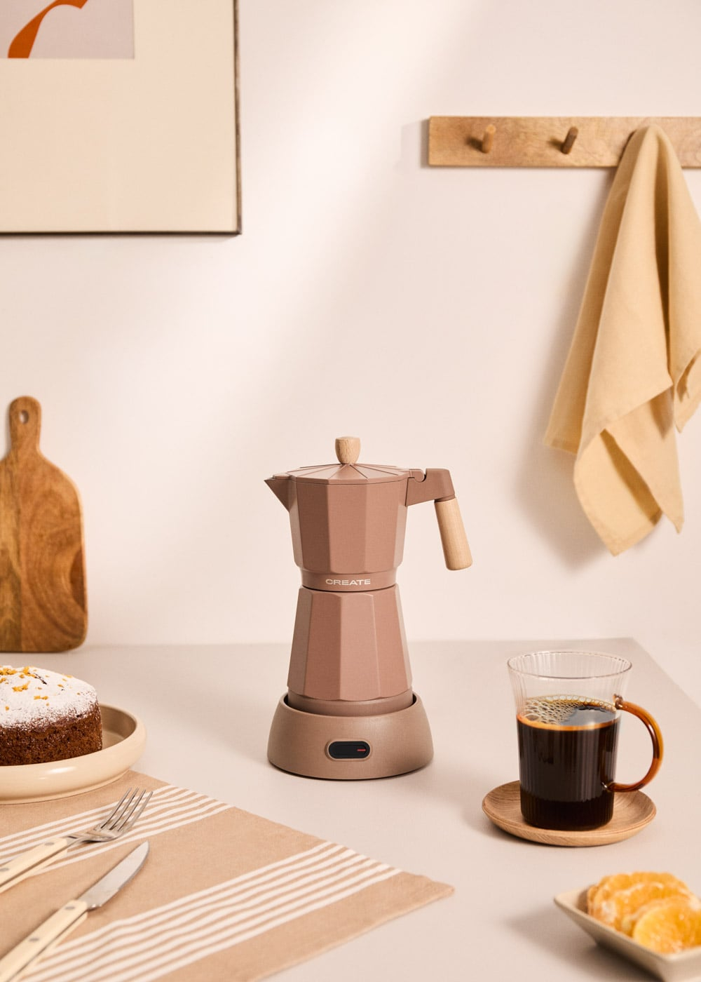 Una cafetera moka marrón junto a café y pastel sobre una mesa.