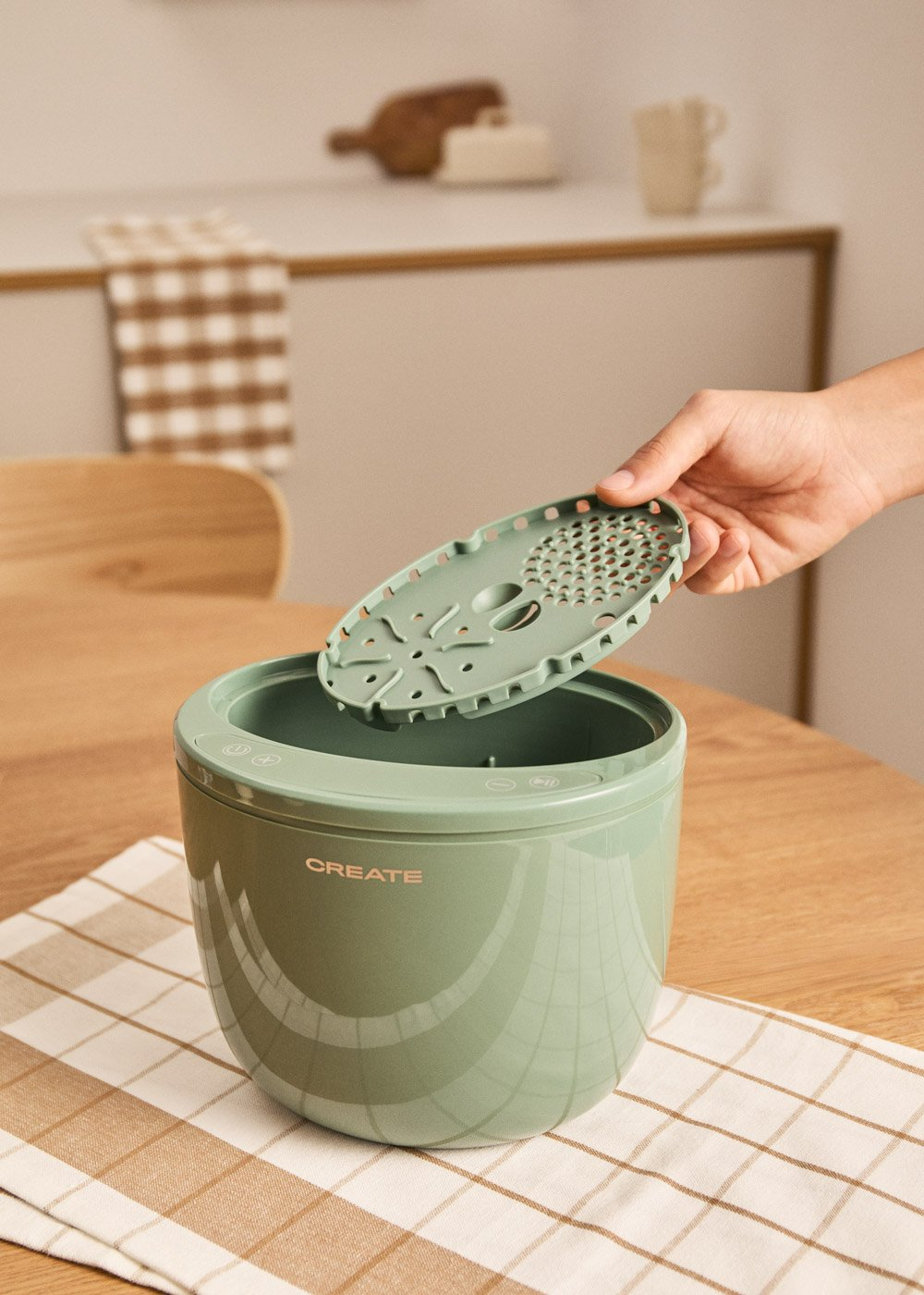 Una mano sostiene un rallador verde sobre un recipiente verde con la etiqueta CREATE.