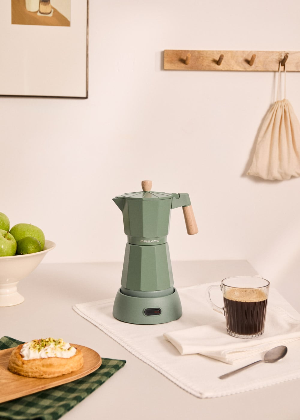 Una cafetera verde junto a una taza de café y un pastel.