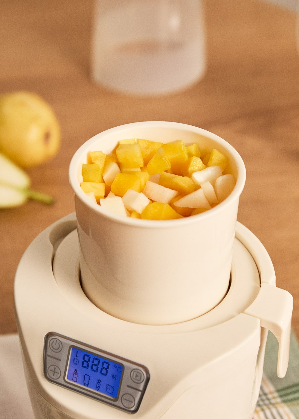 Una taza de fruta en cubos, amarilla y blanca, sobre un aparato con pantalla digital.