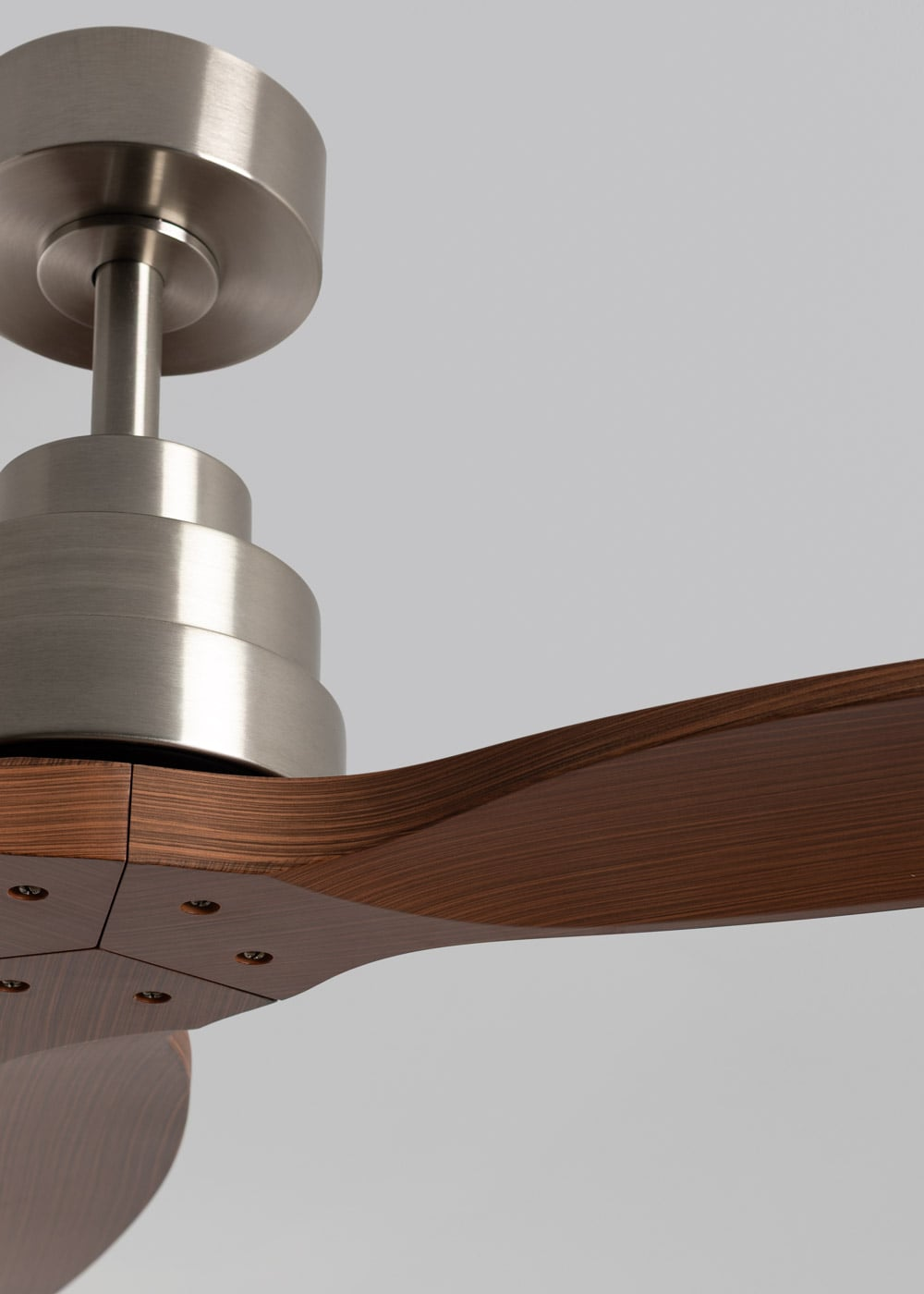 Primer plano de un ventilador de techo moderno con motor de níquel cepillado y aspas de madera.