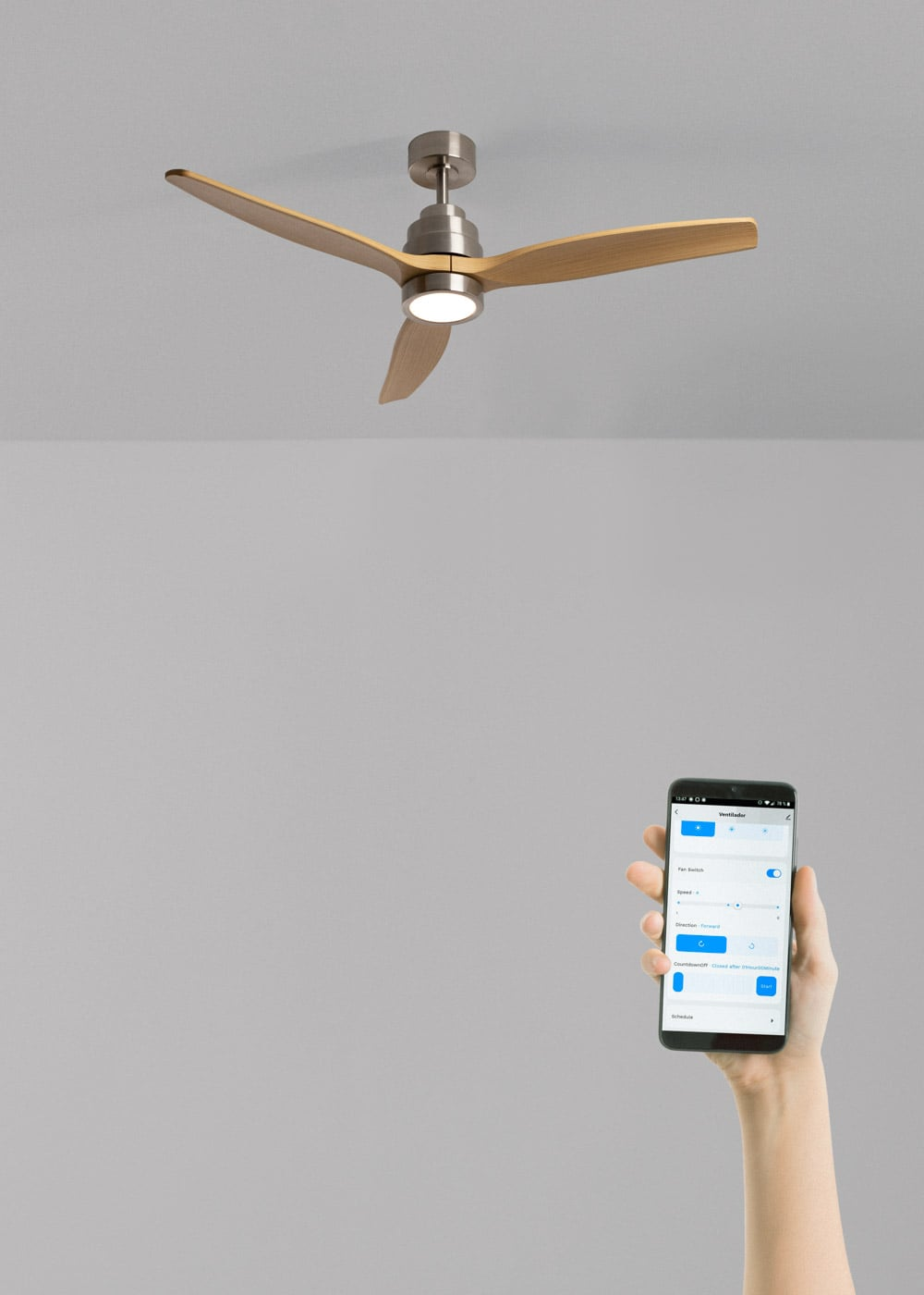 Un ventilador de techo con aspas de madera y luz sobre un smartphone con una app de control.