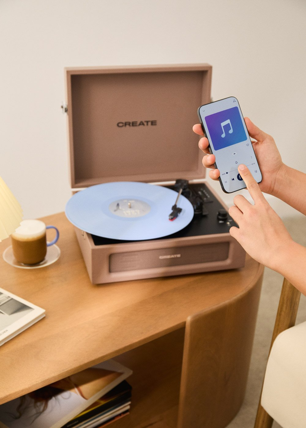 Manos operan un teléfono con app de música cerca de un tocadiscos con vinilo azul.