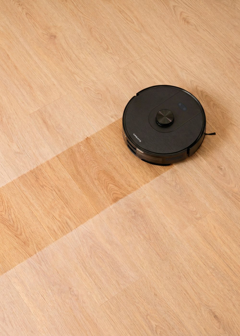 Un robot aspirador negro limpia un suelo de madera, dejando un rastro limpio.