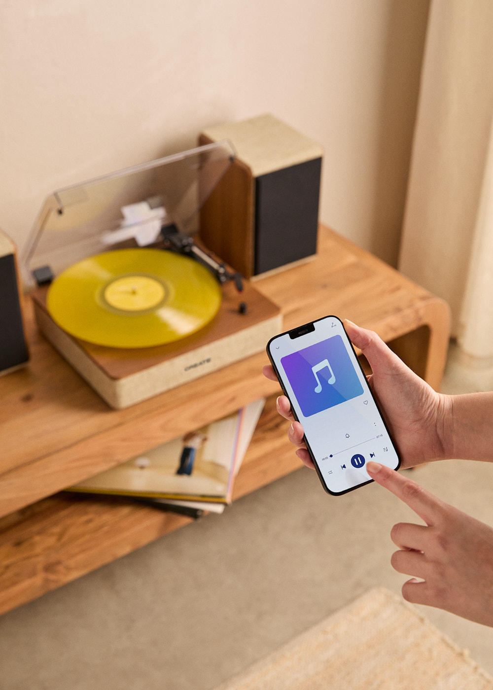Un teléfono muestra una app de música. Al fondo, un tocadiscos con disco de vinilo amarillo.