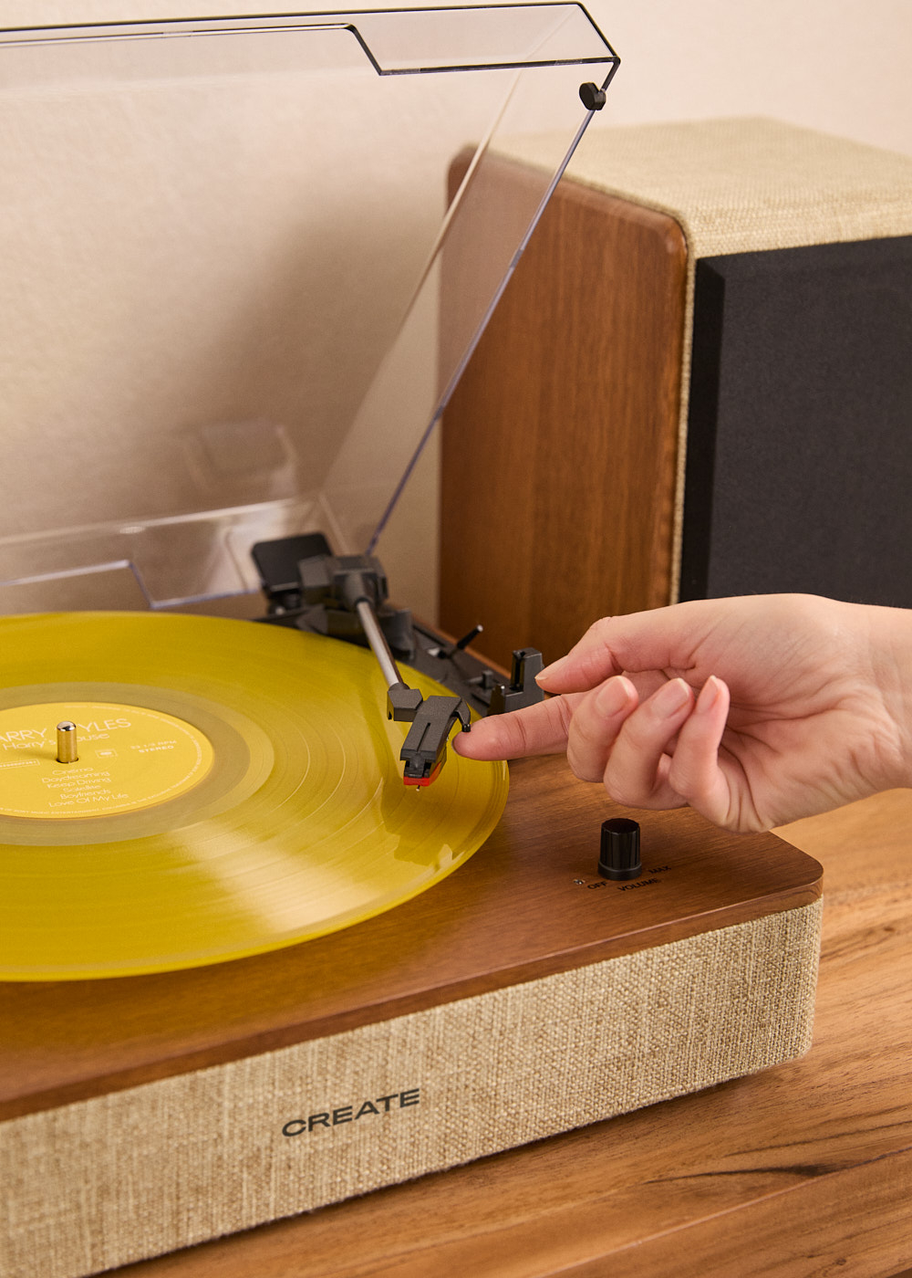 Una mano baja la aguja de un tocadiscos sobre un disco de vinilo amarillo.