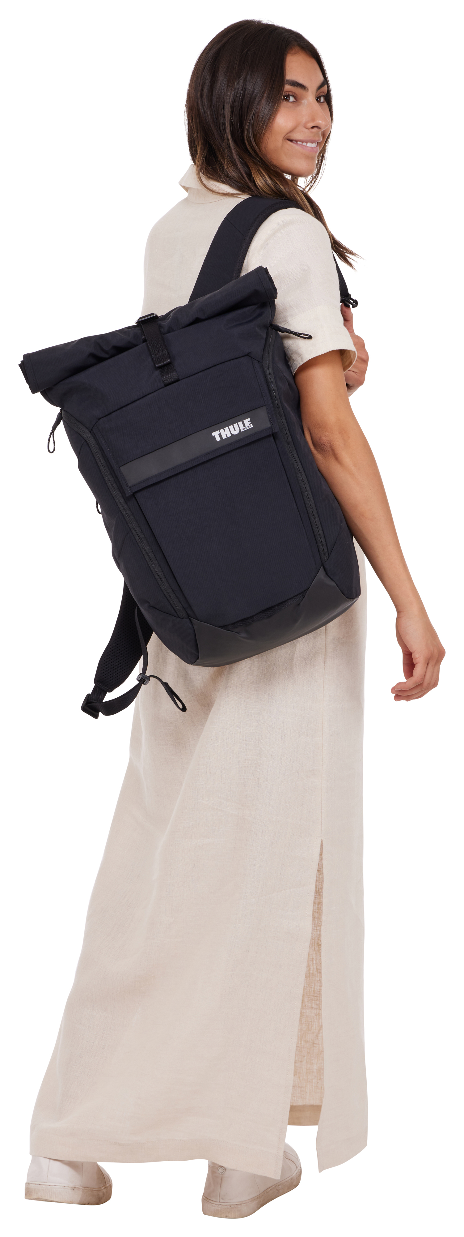 Eine Frau mit dunklen Haaren trägt einen schwarzen Rucksack und ein beiges Kleid.