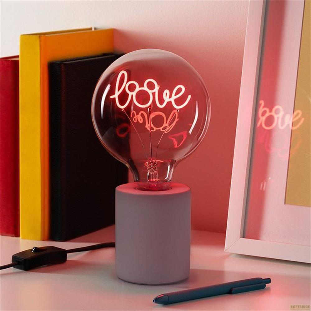 Una lampadina rossa con scritto "love" poggia su una base grigia accanto ai libri.