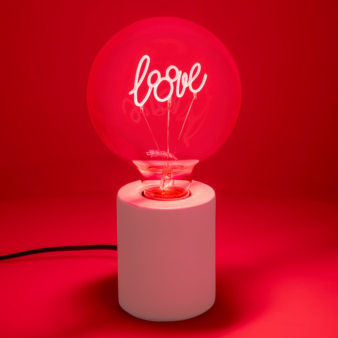 Una lampadina rossa con la parola "amore" si accende su una base bianca.