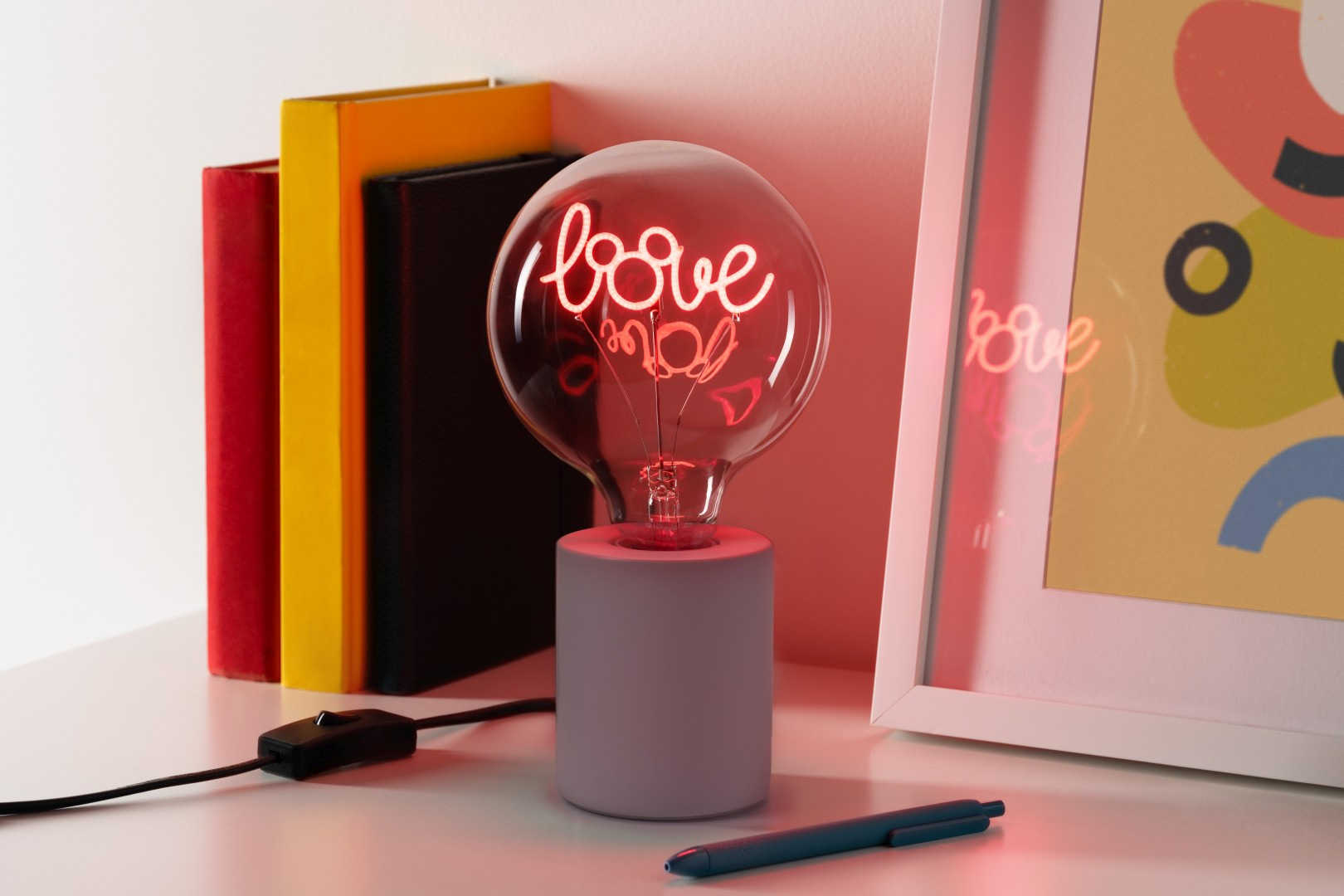 Un comodino con libri, una lampada con la scritta 'love' e un quadro.