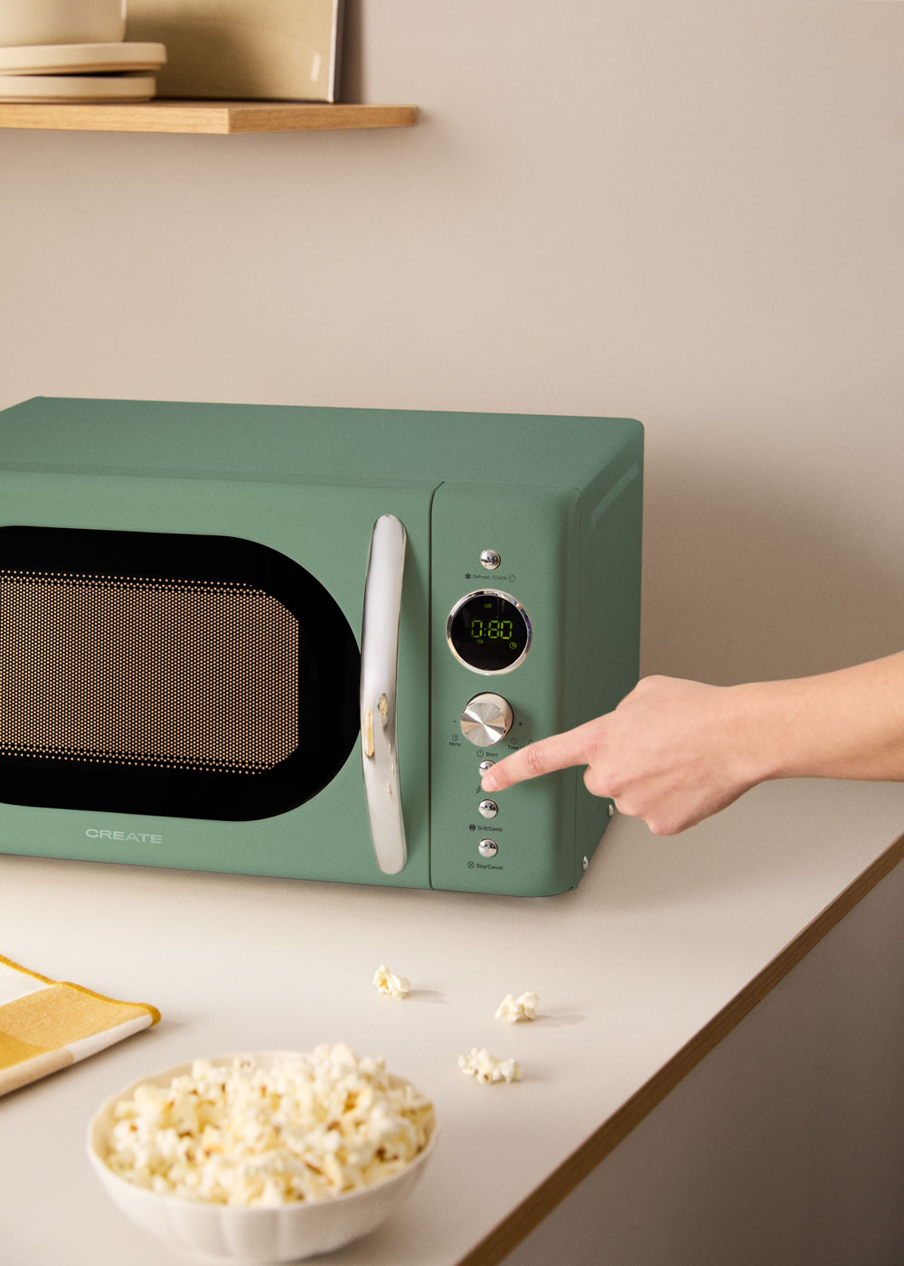 Microondas verde con palomitas en la encimera. Un dedo pulsa inicio.