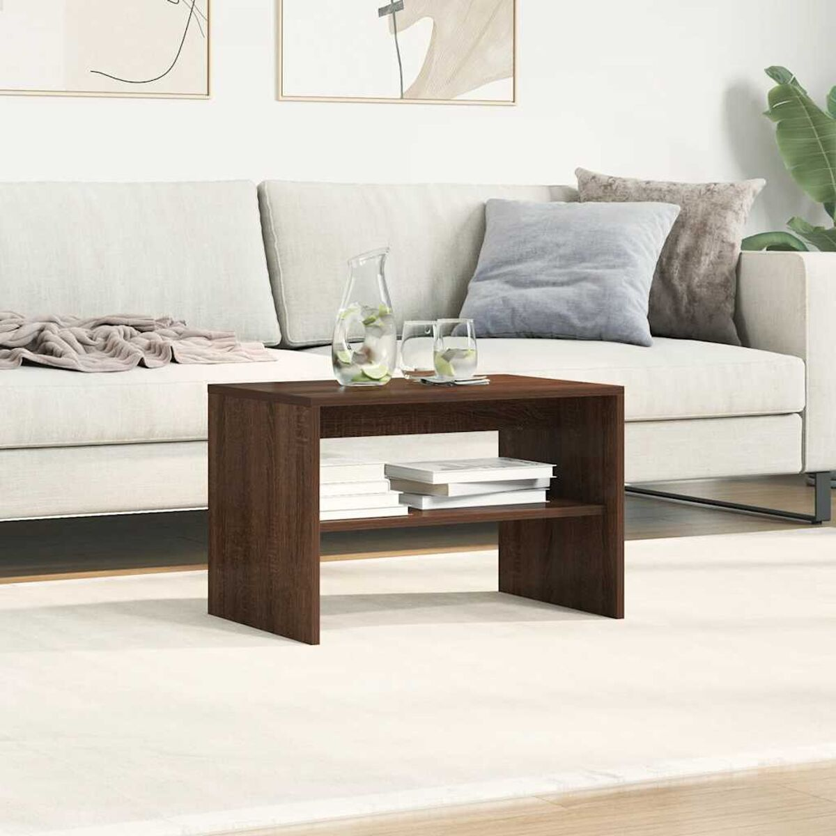 Una mesa de madera oscura con libros se sienta frente a un sofá blanco con cojines y una jarra de agua.